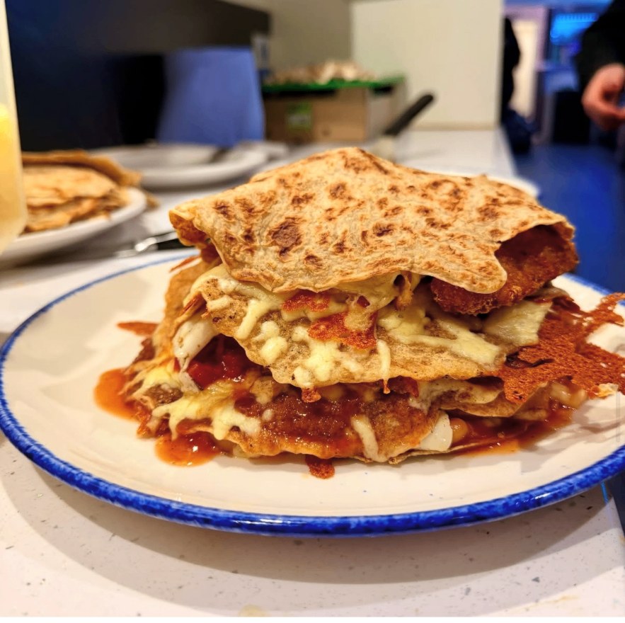 A stack of loaded Staffordshire oatcakes with cheese and sauce
